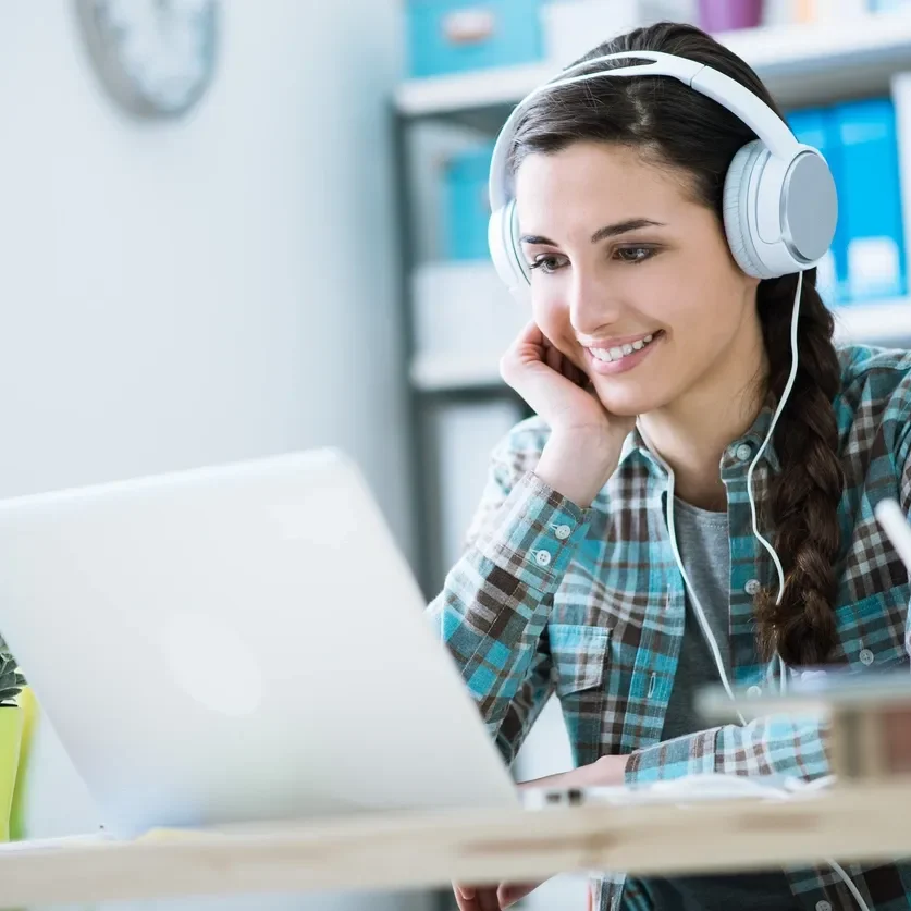 Woman smiling while using laptop with headphones.
